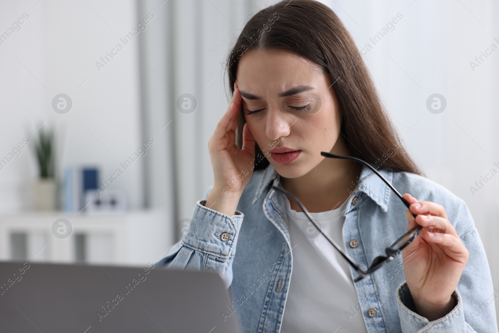 Photo of Woman with glasses suffering from headache at workplace in office