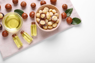 Delicious organic Macadamia nuts, green leaves and natural oil on white background, top view. Space for text