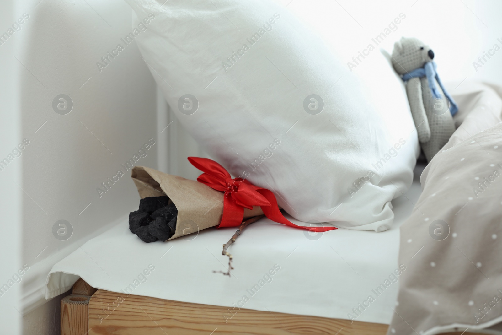 Photo of Wrapped lumps of coal and tree twig under pillow in children's bed. St. Nicholas Day