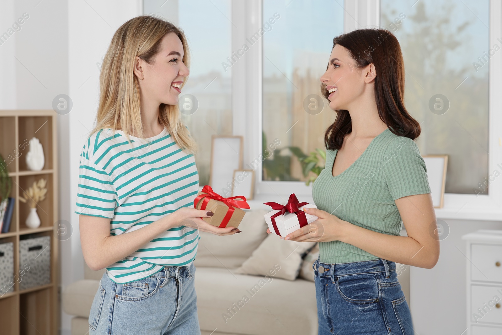 Photo of Smiling young women presenting gifts to each other at home