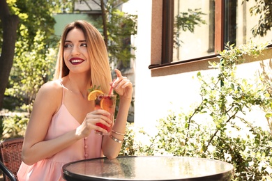 Photo of Young woman with glass of tasty lemonade at table in cafe, outdoors. Natural detox drink