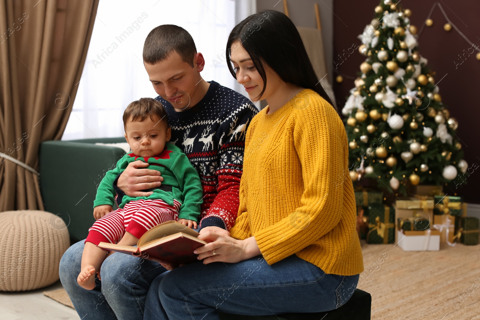 Photo of Parents reading book to their cute son in room decorated for Christmas