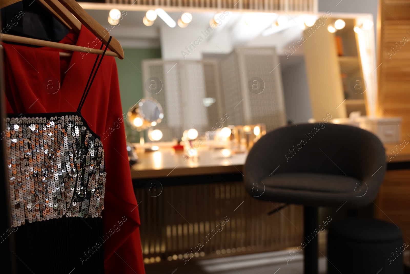 Photo of Makeup room. Chair near dressing table with stylish mirror indoors, focus on clothes rack