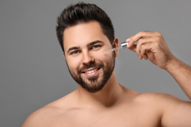 Photo of Handsome man applying cosmetic serum onto face on grey background