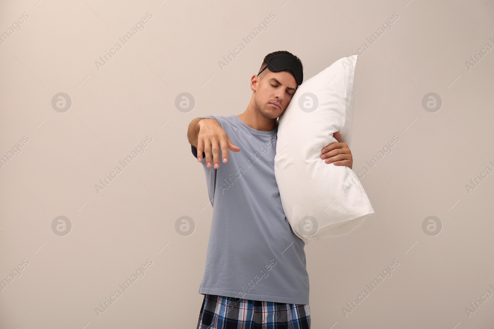 Photo of Somnambulist with soft pillow on beige background. Sleepwalking