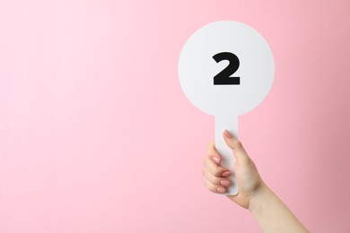 Woman holding auction paddle with number 2 on pink background, closeup. Space for text