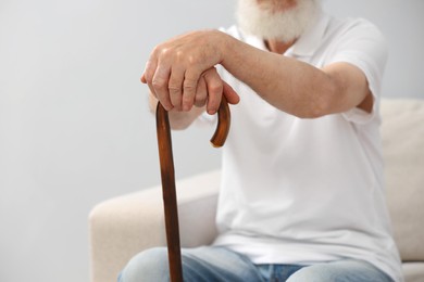 Photo of Senior man with walking cane on sofa indoors, closeup