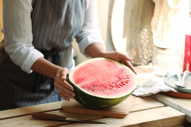 Photo of Woman holding half of fresh juicy watermelon at wooden table, closeup