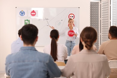 Photo of Teacher showing Stop road sign near whiteboard during lesson in driving school