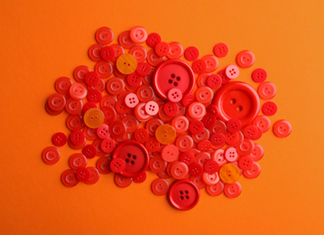 Photo of Many red sewing buttons on orange background, flat lay