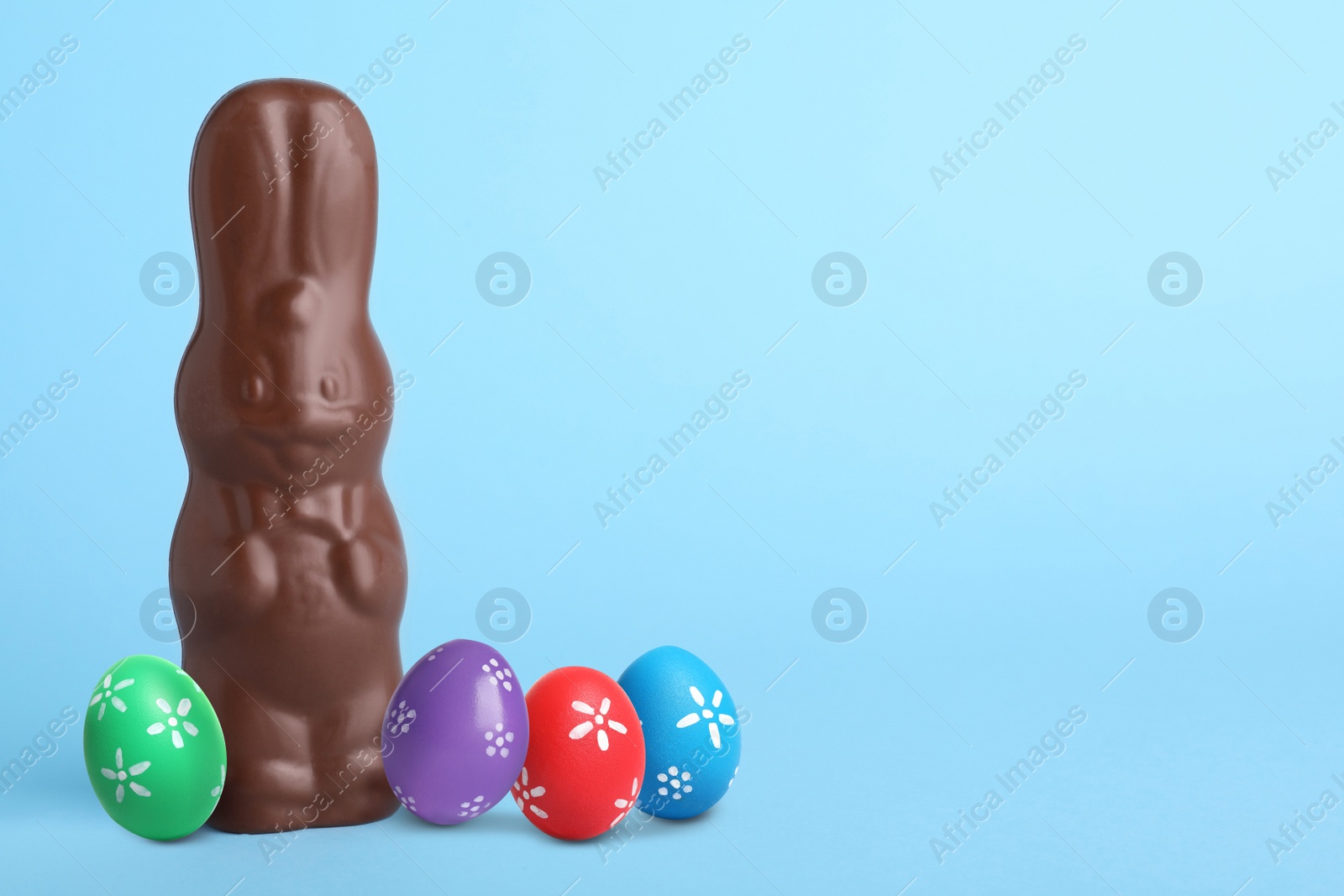 Image of Chocolate bunny and painted Easter eggs on light blue background, space for text