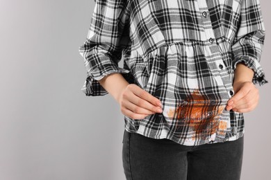 Woman showing stain from sauce on her shirt against light grey background, closeup. Space for text