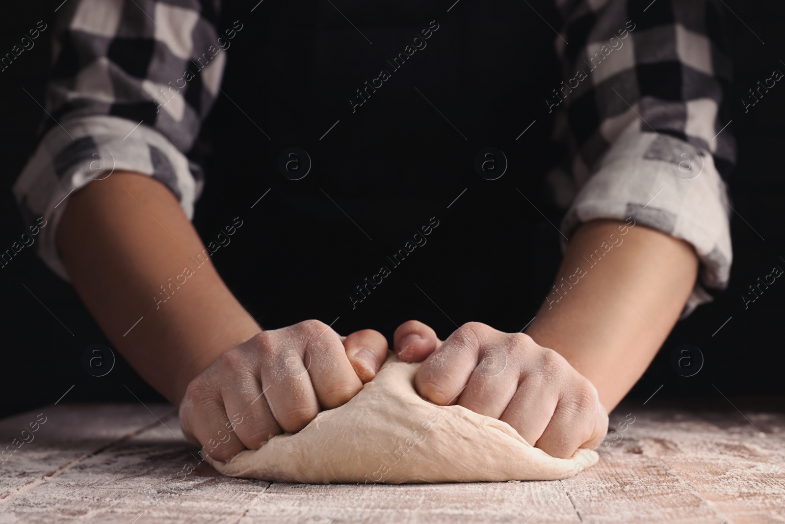 Photo of Man kneading dough at wooden table on dark background, closeup