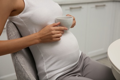 Beautiful pregnant woman drinking tea in kitchen, closeup