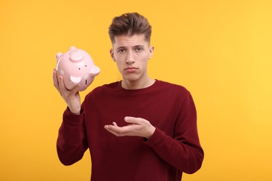 Photo of Upset man with empty piggy bank on yellow background