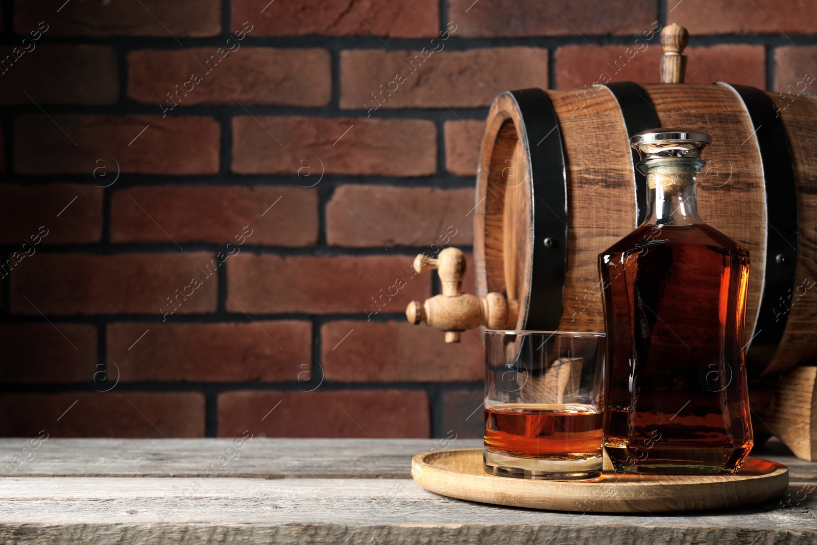 Photo of Golden whiskey and barrel on wooden table against brick wall, space for text