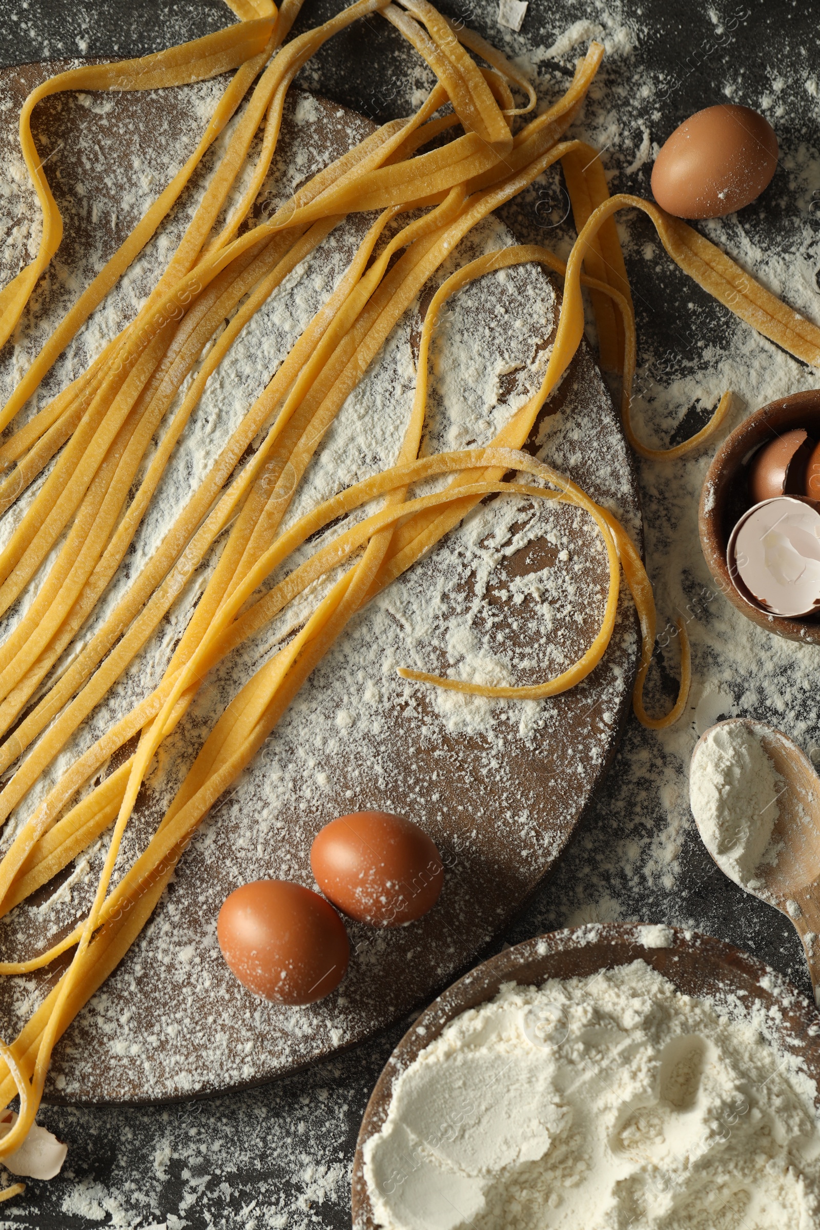 Photo of Homemade pasta, flour and eggs on dark table, flat lay