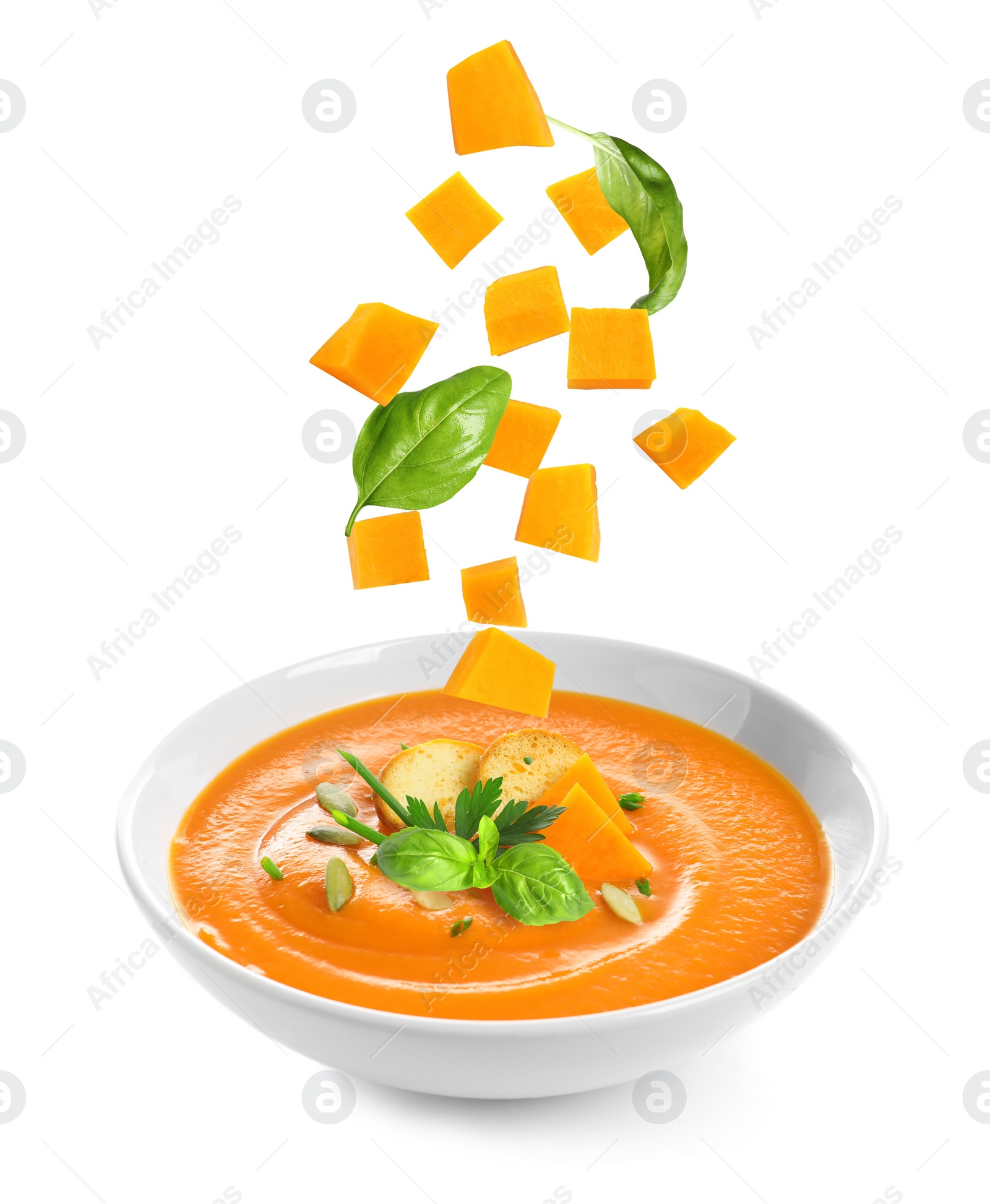 Image of Ingredients falling into bowl of homemade pumpkin soup on white background 