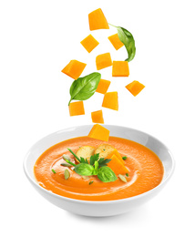 Image of Ingredients falling into bowl of homemade pumpkin soup on white background 