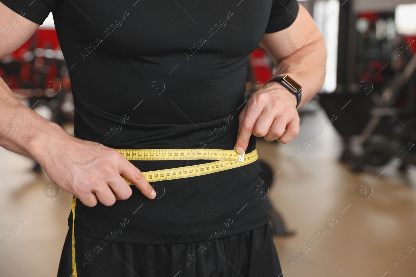 Photo of Athletic man measuring waist with tape in gym, closeup