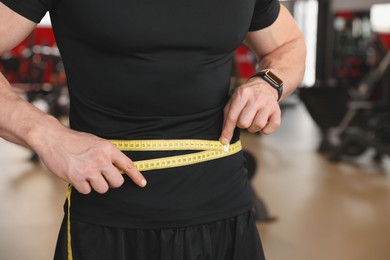 Photo of Athletic man measuring waist with tape in gym, closeup