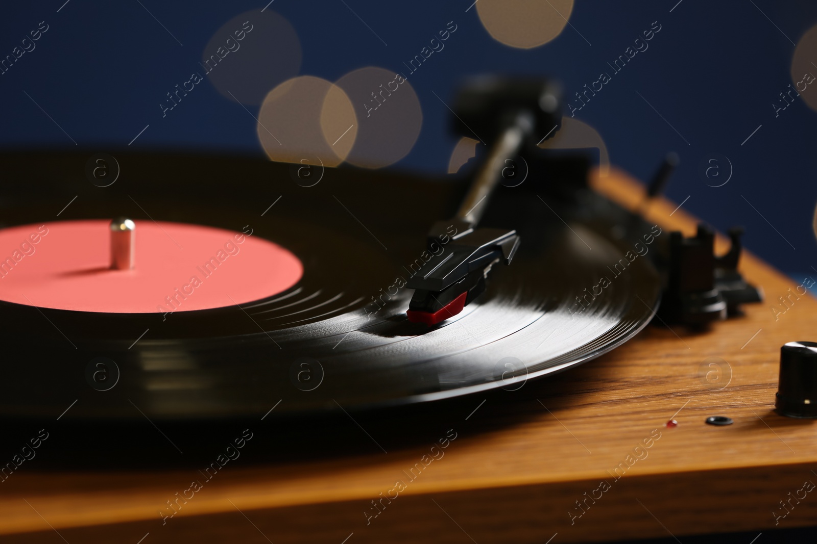 Photo of Vinyl record on turntable against blurred lights, closeup