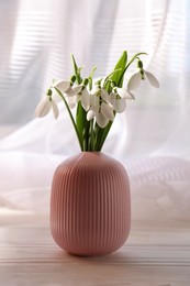 Beautiful snowdrops in vase on white wooden table indoors