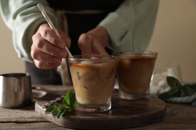 Photo of Woman stirring iced coffee with straw at wooden table, closeup