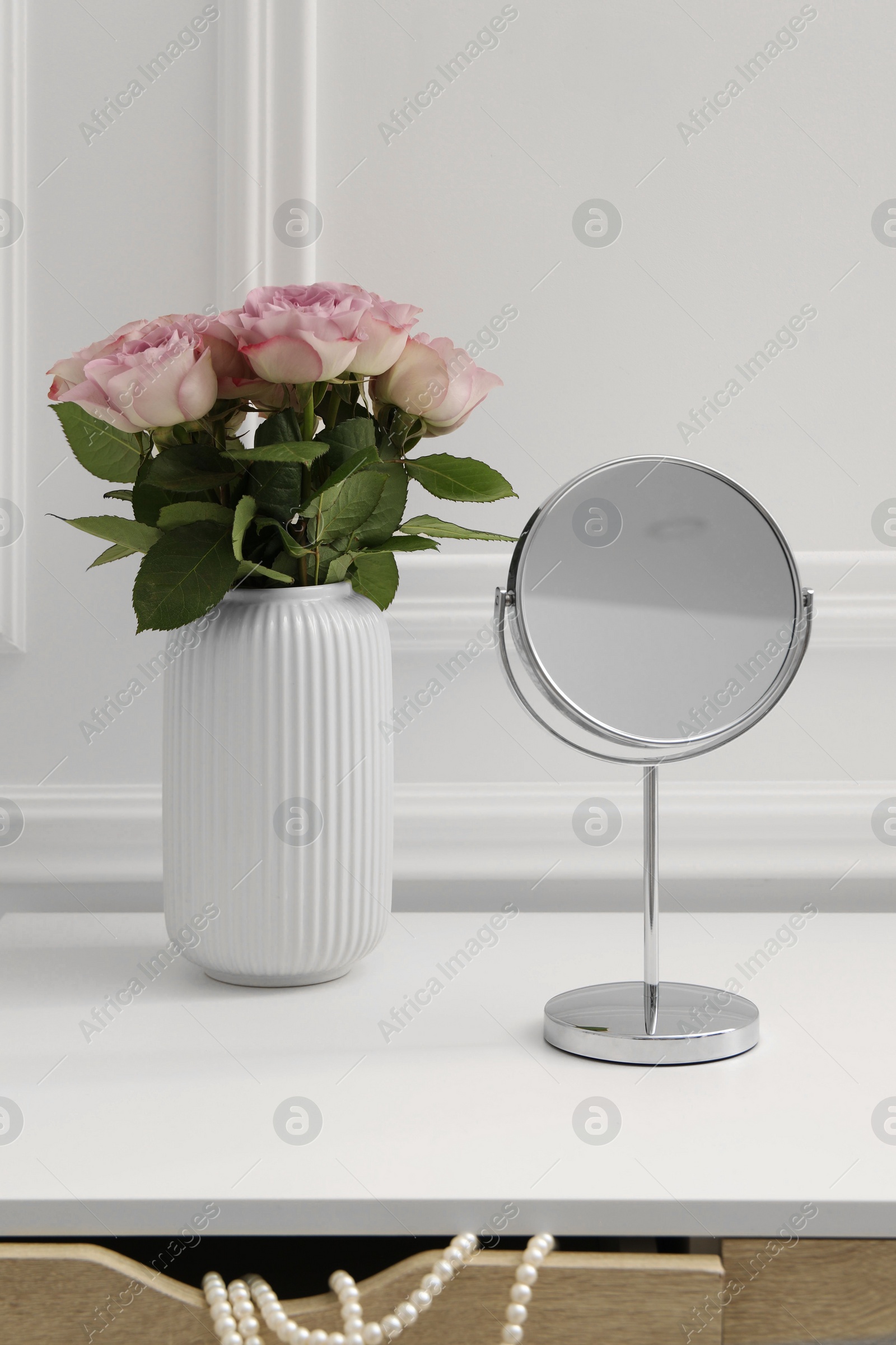 Photo of Mirror and vase with pink roses on white dressing table in makeup room