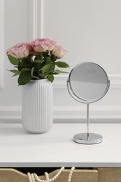 Photo of Mirror and vase with pink roses on white dressing table in makeup room