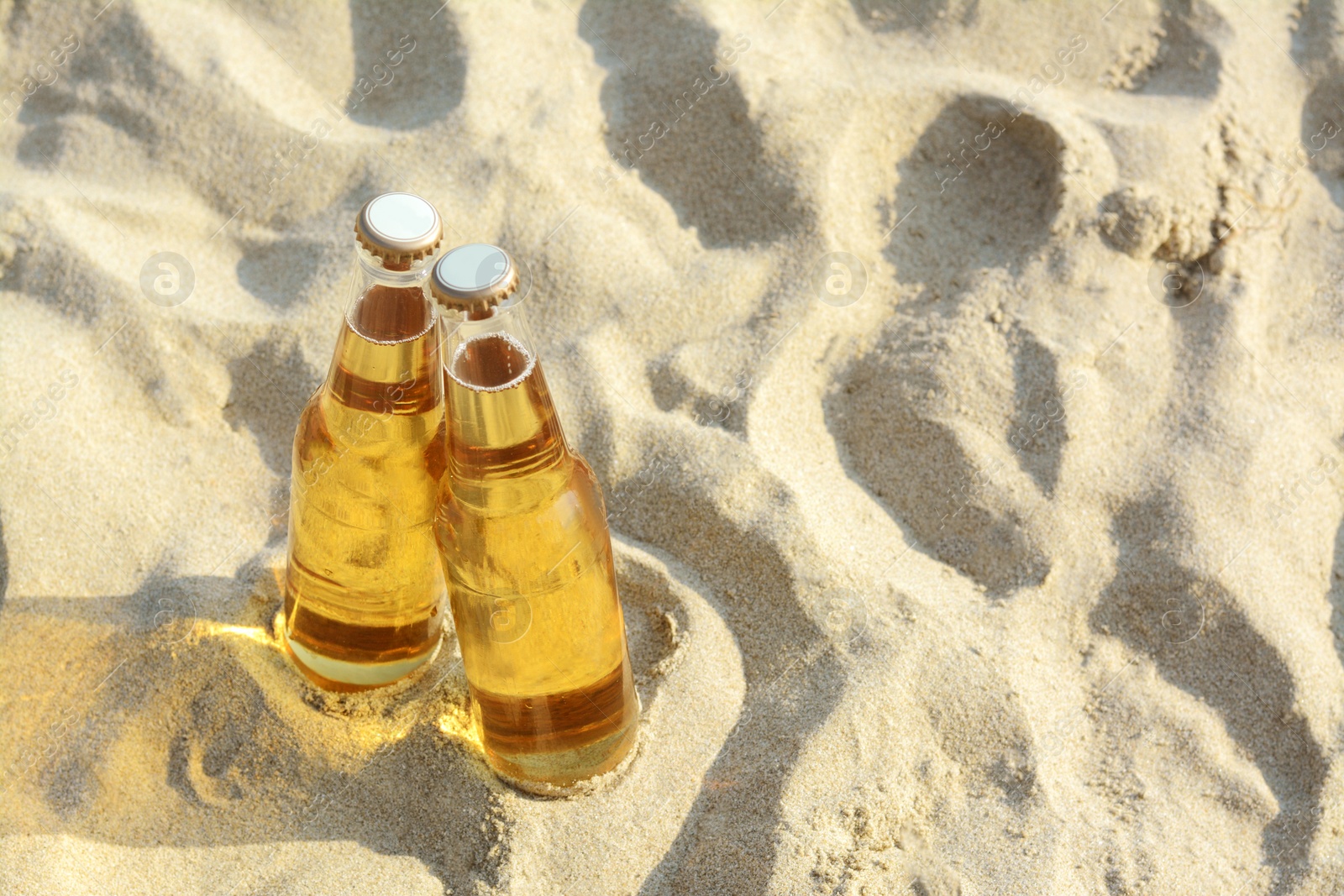 Photo of Bottles of cold beer on sandy beach, above view. Space for text