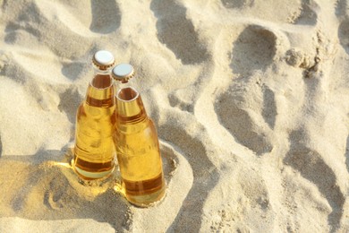 Bottles of cold beer on sandy beach, above view. Space for text