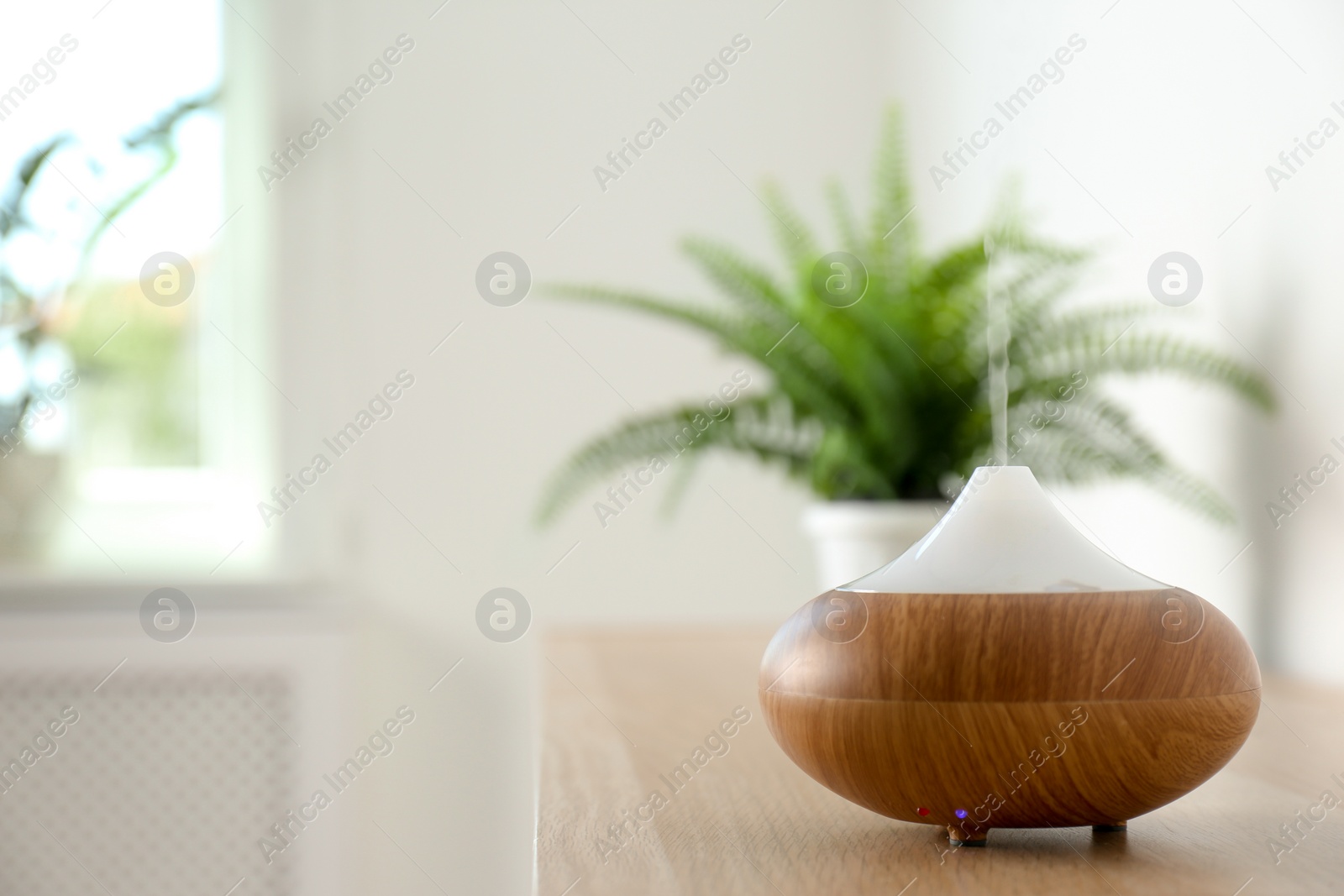 Photo of Modern aroma lamp on table against blurred background with space for text