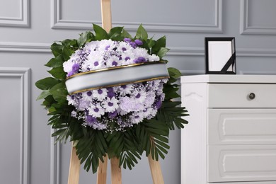 Wreath of violet and white flowers, photo frame with black ribbon in room. Funeral attributes