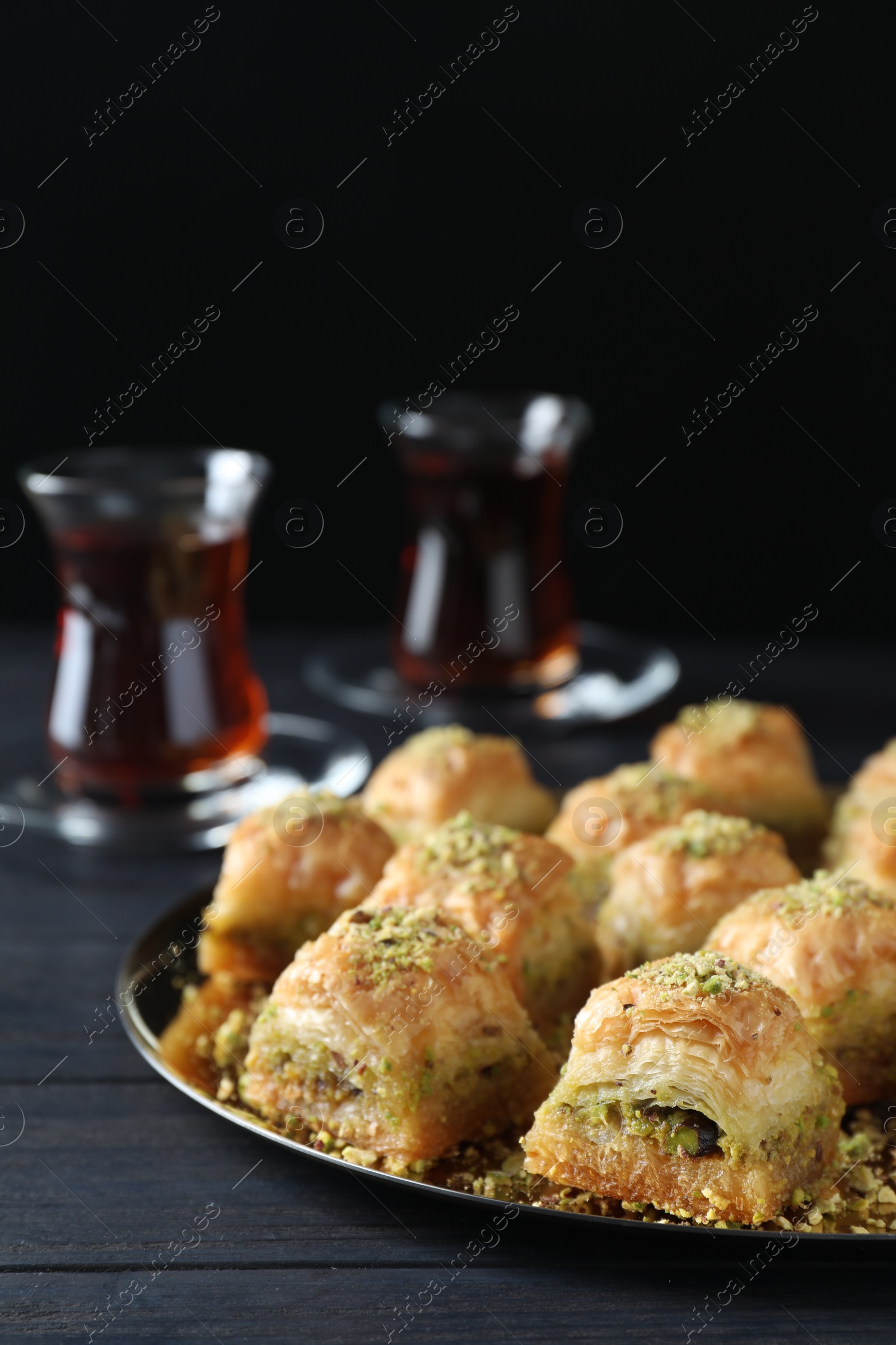 Photo of Delicious fresh baklava with chopped nuts on black wooden table, closeup. Eastern sweets