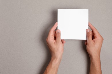 Man holding sheet of paper on grey background, closeup. Mockup for design