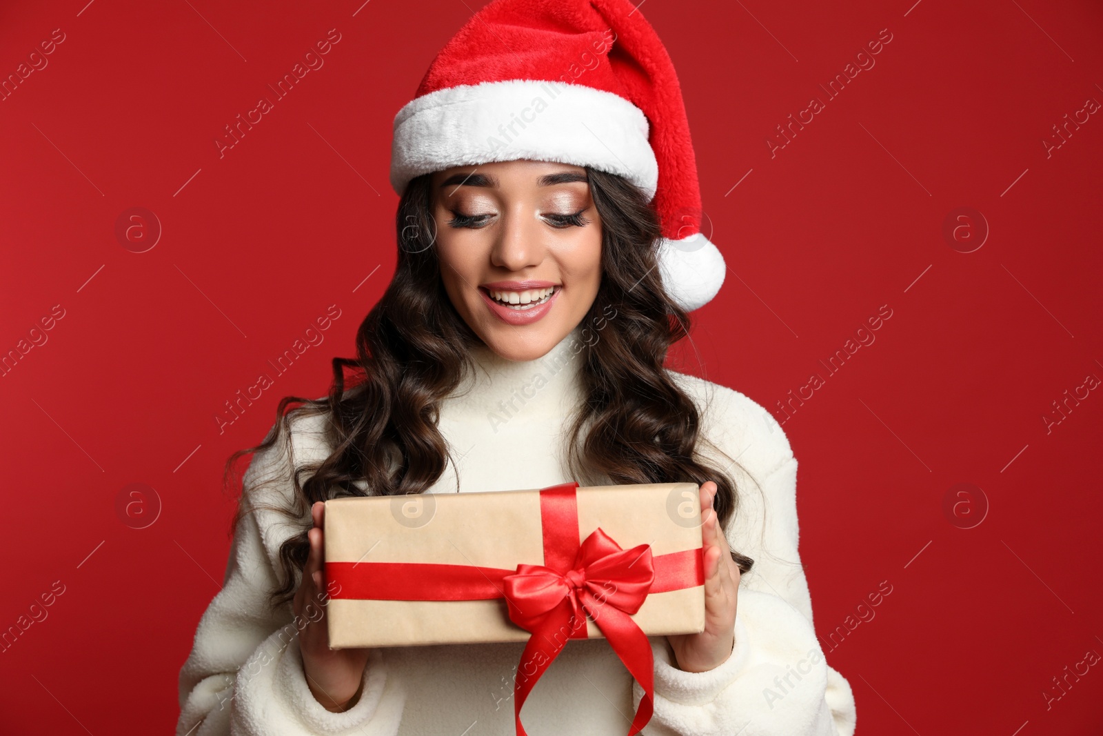 Photo of Beautiful woman in Santa hat with Christmas gift on red background