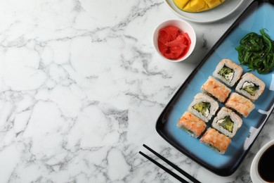 Photo of Delicious sushi rolls served on white marble table, flat lay. Space for text