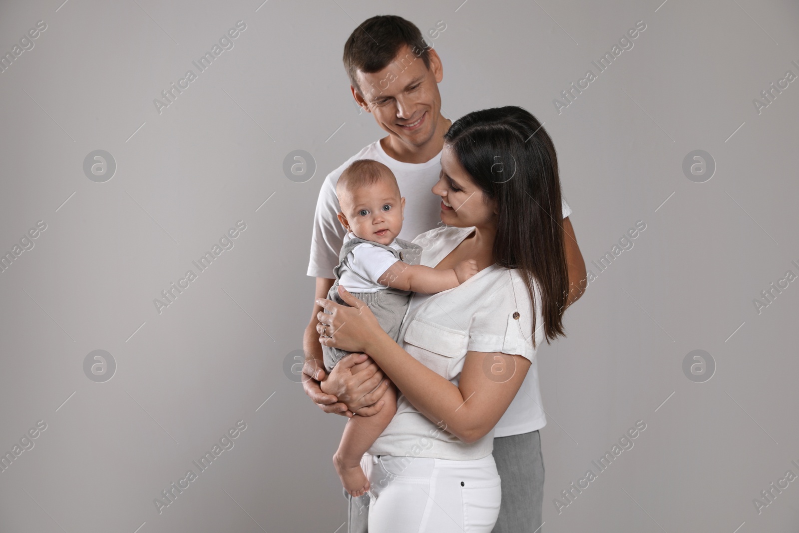 Photo of Happy family. Couple with their cute baby on grey background