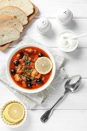 Photo of Meat solyanka soup with sausages, olives and vegetables served on white wooden table, flat lay