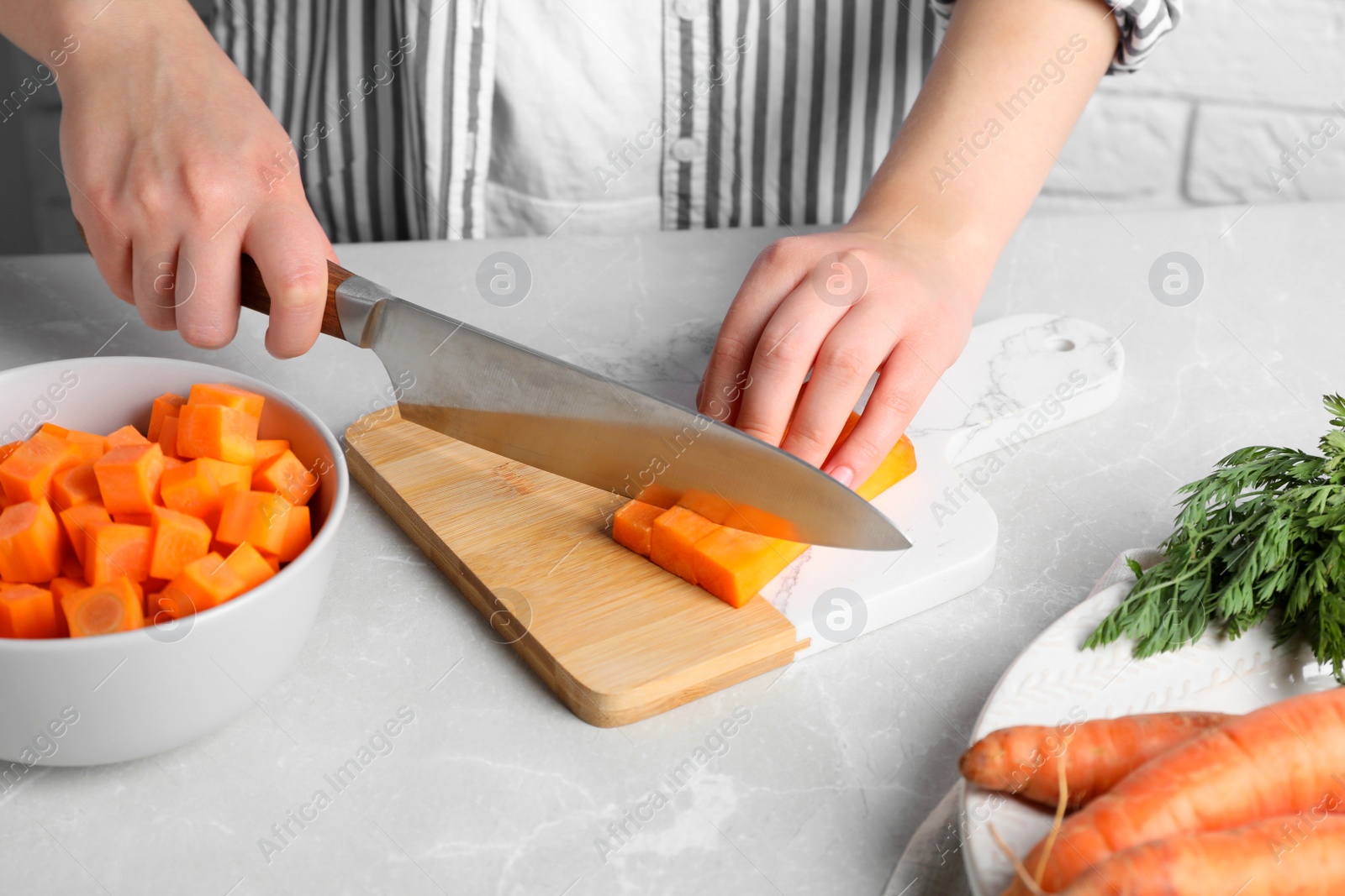 Photo of Woman cutting fresh ripe juicy carrots at light grey table, closeup