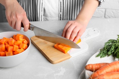 Woman cutting fresh ripe juicy carrots at light grey table, closeup