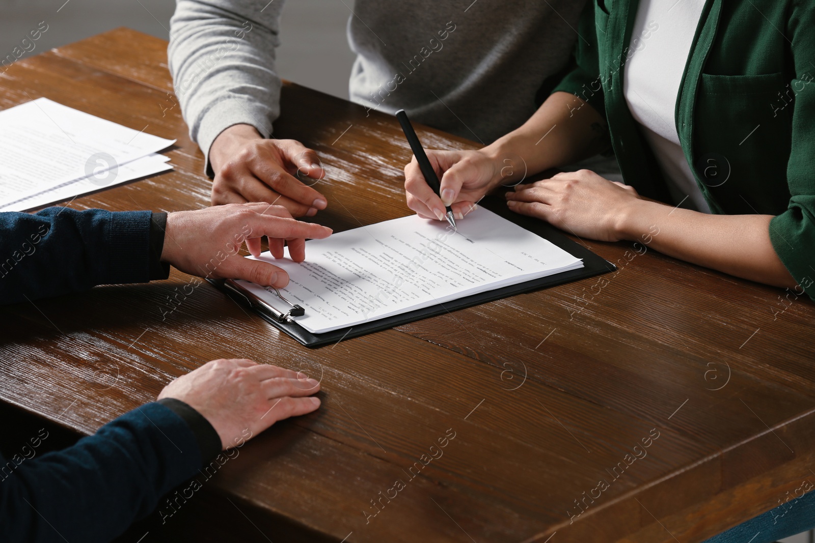 Photo of Notary helping couple with paperwork at wooden table, closeup