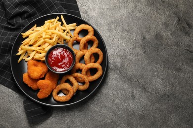 Plate with tomato ketchup and different snacks on grey textured table, top view. Space for text