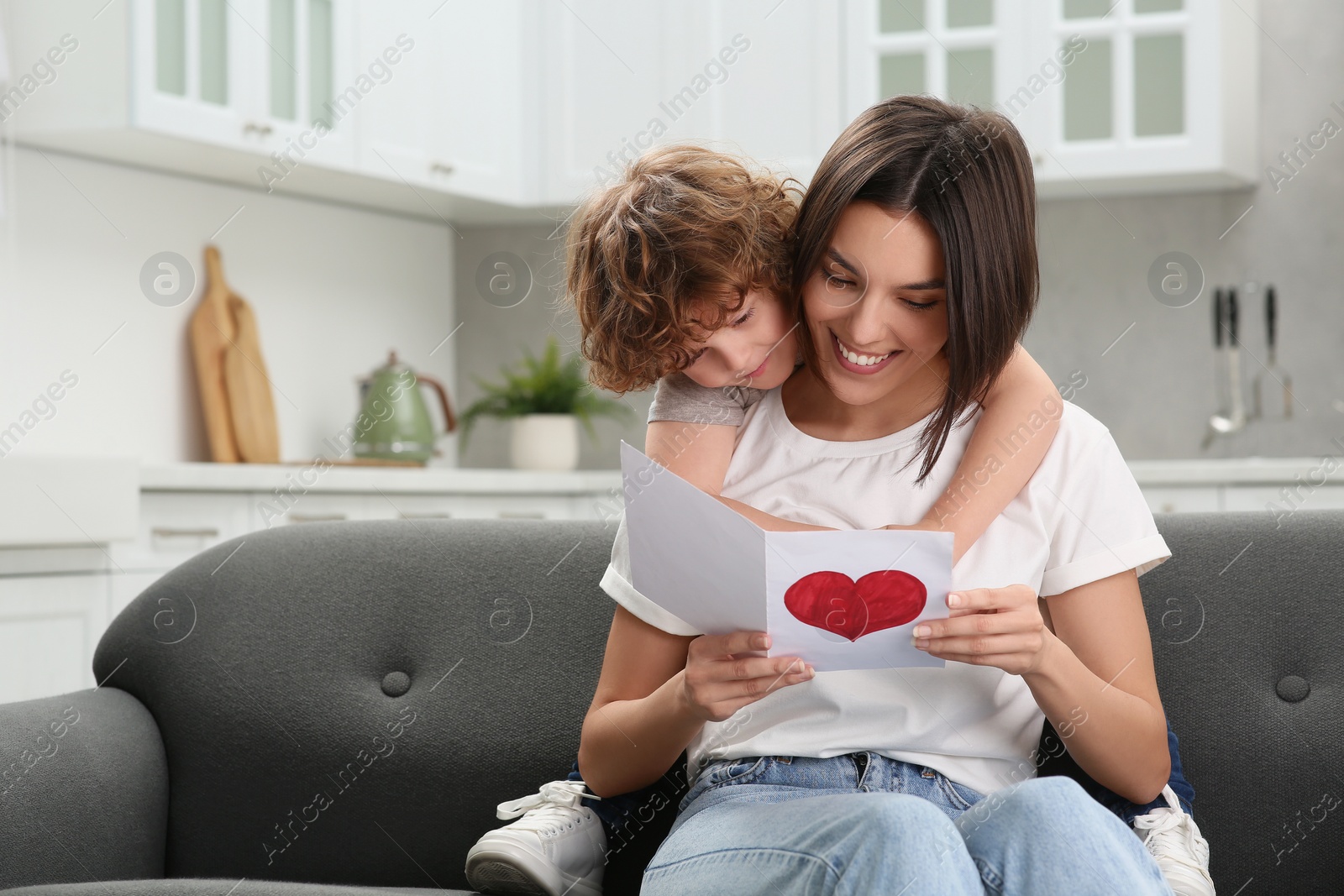 Photo of Little son congratulating his mom with Mother`s day at home. Woman holding greeting card