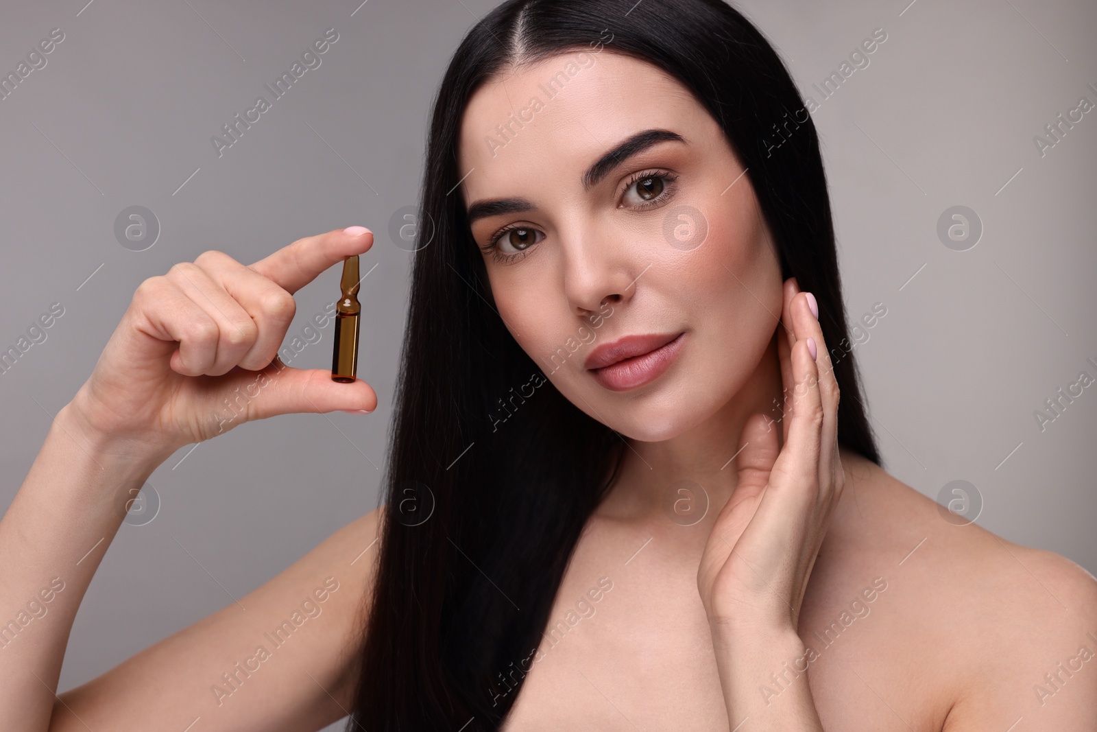 Photo of Beautiful young woman holding skincare ampoule on grey background