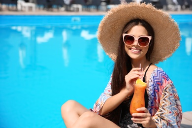 Photo of Beautiful young woman with cocktail sitting near outdoor swimming pool
