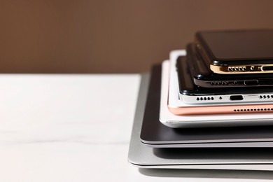 Many different modern gadgets on white table against brown background, closeup. Space for text