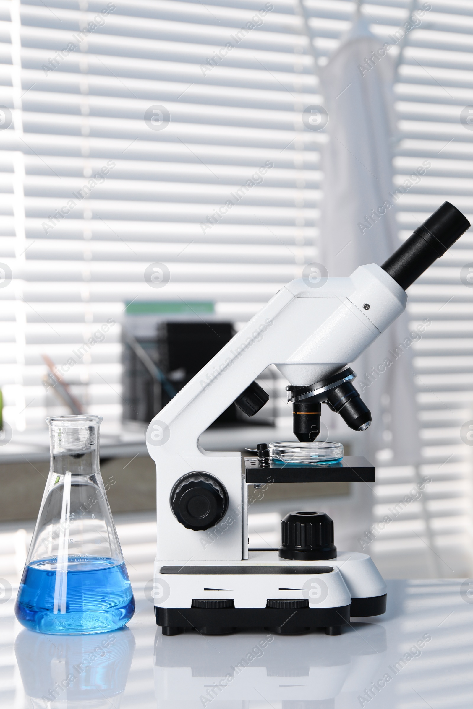 Photo of Laboratory analysis. Flask with blue liquid and microscope on white table indoors