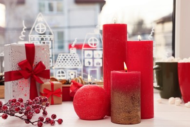 Beautiful burning candles with Christmas decor on white wooden table near window